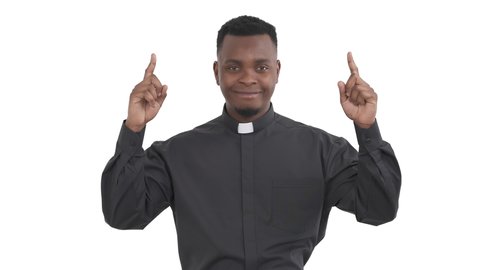 Portrait of satisfied African priest pointing fingers up and joyfully nodding his head isolated on white background.