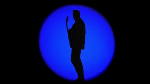 Shadow of an unrecognizable guitarist in a round beam of blue light. Musician playing a rhythm guitar