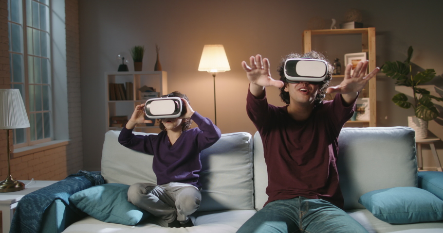 Funny south asian siblings or father and son with curly hair are trying virtual reality headsets, having fun playing video games - modern technologies, family time concept 4k footage