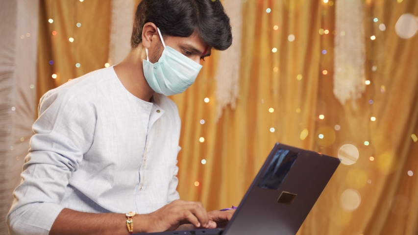 young man with medical mask making video call and showing Rakhi or Raksha Bandhan to his sister or family friends after festival ceremony during coronavirus ot covid-19 pandemic. Royalty-Free Stock Footage #1056392831