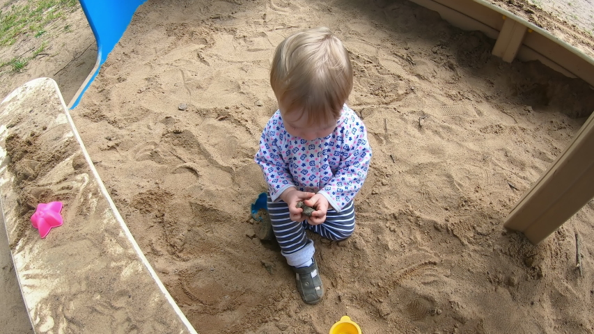 Funny little blond boy sitting on the sand in the sandbox, playing with toys on the Playground on a clear Sunny day. Happy childhood.