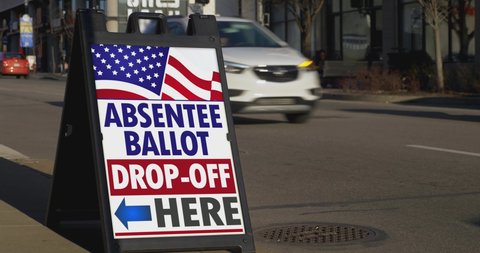 A sign on the sidewalk of a large city shows where to drop off absentee ballots.  	