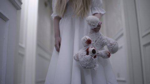 Possessed girl in white dress holding bloody toy, horrible sacrifice ritual