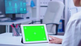 Tablet pc with green screen in hospital cabinet used by doctor wearing white coat. Nurse in blue uniform entering in clinic. Doctor in health clinic working on tablet computer with replaceable screen - Powered by Shutterstock - Get 15% off with code: PIKWIZARD15