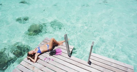 Tropical paradise travel holidays woman enjoying sun lying down sunbathing after snorkel swim from luxury overwater bungalow villa private terrace in idyllic getaway.