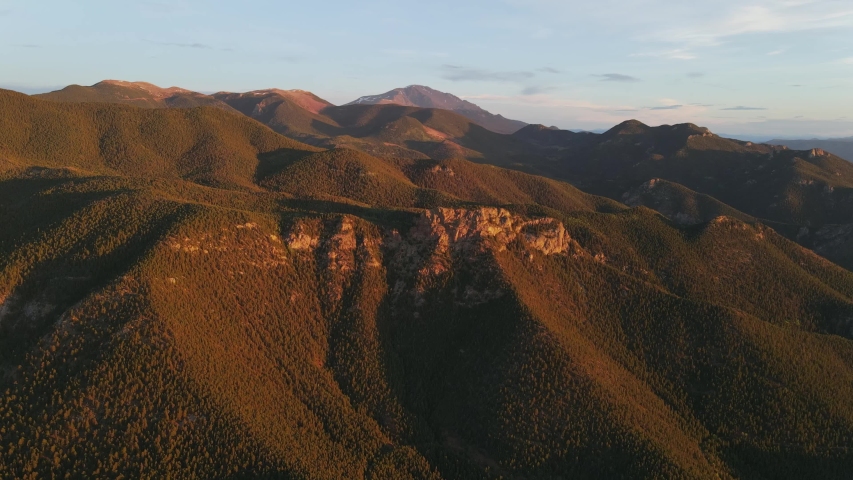Aerial view slow moving shot, Scenic view of mountain ranges in Pikes Peak National Forest, blue sky in the background.