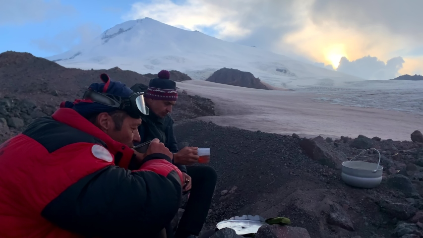 Climbers - travelers sit drinking tea with chocolates at the foot of Elbrus. Aerial view of a beautiful mountain winter landscape.