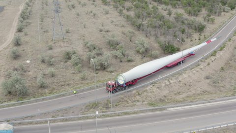 Aerial footage of a huge truck loaded with a blade of a wind turbine rides along the roundabout