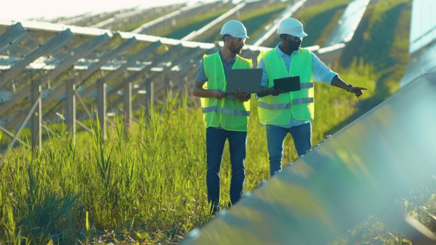 Close up engineers use laptop and project plan on the solar farm in special uniform standing look around discuss the installation of sunny batteries electricity environmental slow motion Royalty-Free Stock Footage #1056411968