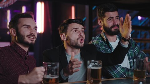 Three guys charismatic closeup to the camera football fans in a pub while drinking beer watching the match they are so emotional in a sport bar