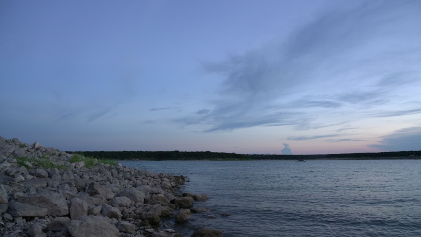 View of Boats on Large Lake From Rocky Shoreline At Dusk