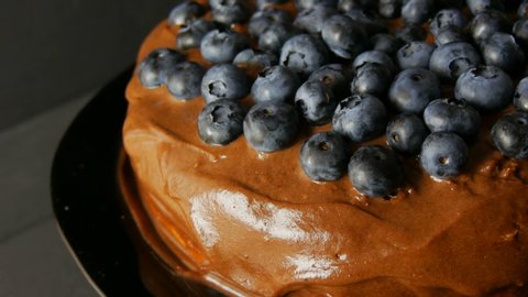 Close up view of brownie chocolate pie with cocoa frosting and blueberries on stylish black background in low key.