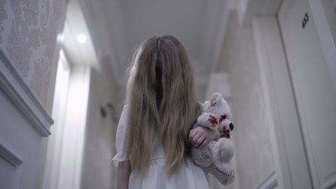 Strange little girl holding bloody teddy bear, face hidden in hair, horror story
