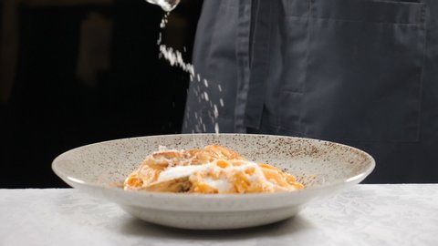 Male chef putting parmesan cheese on pasta in slow motion. Sprinkling pasta with grated cheese. Cooking in restaurant, Chef serves cooked macaroni in restaurant on the table. Full hd