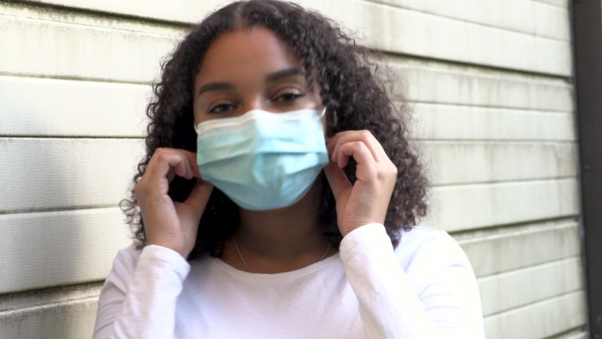Beautiful mixed race African American girl biracial teenager young woman outside wearing and removing a face mask during COVID-19 Coronavirus pandemic | Shutterstock HD Video #1056418460