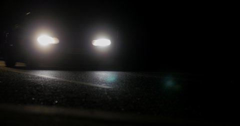 Cars at night filmed from low down on the roadside, headlights passing in a loop