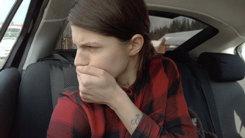 Woman sits in the back seat of a car and feels bad. Female vomiting in the back seat of a car. Covers her mouth with her hand