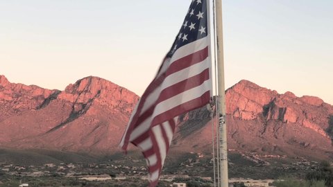 American flag blows gently in wind in front of mountains at sunset, close up