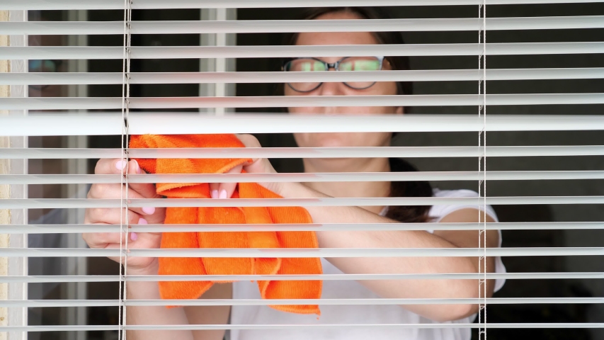 Young woman washing white blinds.
