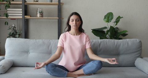 Mixed race Indian woman sit cross-legged on comfy sofa in living room closed eyes do meditation practice feels inner harmony and balance, improve self-conscious, mindfulness state, no stress concept