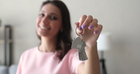 Close up focus female hand holding showing to camera bunch of keys with home shaped keychain on background smiling indian mixed race woman. New home, tenancy, real estate agent offer new house concept