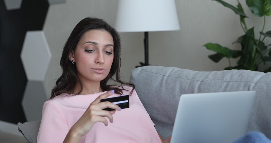 Mixed race Indian woman sit lean on sofa use laptop hold credit card having unsuccessful e-payment feel puzzled. Financial troubles, card is declined, debt, late or missing payment, scam fraud concept Royalty-Free Stock Footage #1056430187
