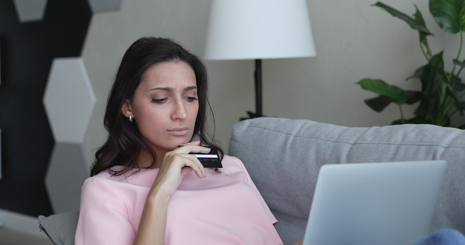Mixed race Indian woman sit lean on sofa use laptop hold credit card having unsuccessful e-payment feel puzzled. Financial troubles, card is declined, debt, late or missing payment, scam fraud concept Royalty-Free Stock Footage #1056430187