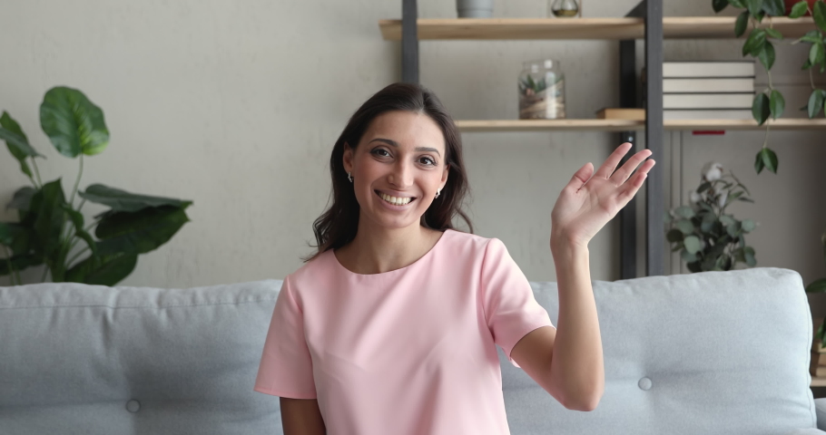 Indian woman sit on sofa at home wave hand greet interlocutor start video call distant communication. Female applicant candidature pass job interview feels confident, hiring process by videoconference