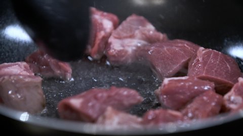 Stir Fry Fresh Raw Cubes of Meat in Hot Black Non Stick Pan with Oil