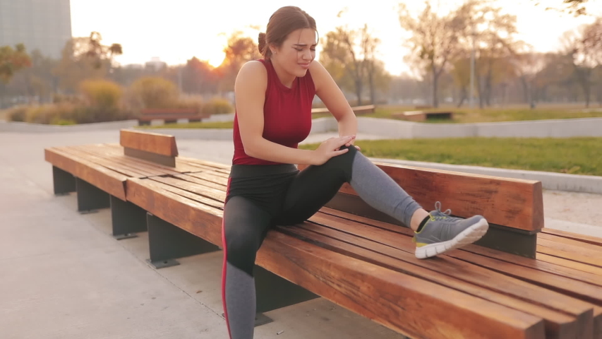 Young sportswoman having pain / injury during exercise and jogging in the park. Royalty-Free Stock Footage #1056430802