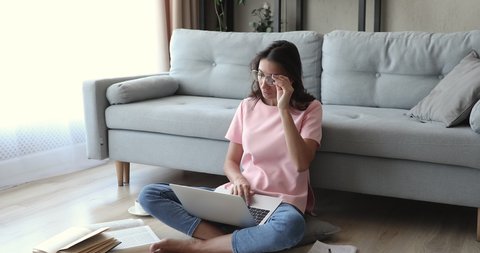 Indian woman sit on floor in living room feel tired after long use work on pc take off glasses reduce eye fatigue discomfort feelings, negative influence of modern tech of health, overworking concept