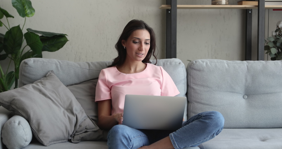 Attractive Indian mixed-race woman relaxing at home sit on comfortable couch using laptop, chatting with friends in social network, spending lazy weekend, do remote job, shopping online, writing email Royalty-Free Stock Footage #1056440009