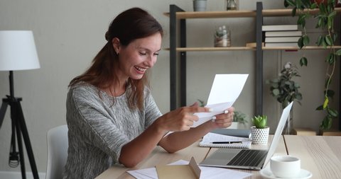 Woman sitting at desk take out official notice from envelope read great positive incredible news in letter feels happy, celebrate achievement at work career advance, overjoyed by admission scholarship