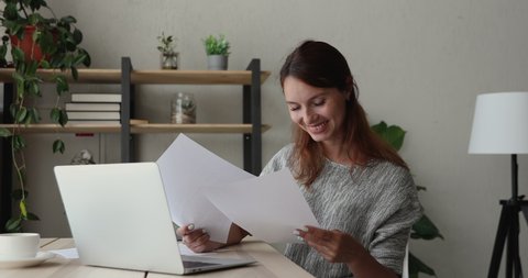 Woman sit at desk using laptop holding financial document, make data analysis, check statistics research, do paperwork during fruitful workday in office. Telework from home, e-pay e-bank user concept