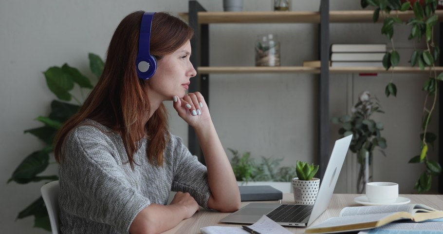 Pensive sad woman in headphones sit at desk in front of laptop thinking, has difficulties, search problem solution, task making, feeling boredom or tired after long studies or exam preparation concept Royalty-Free Stock Footage #1056440057