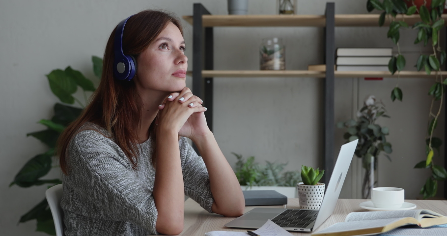 Pensive sad woman in headphones sit at desk in front of laptop thinking, has difficulties, search problem solution, task making, feeling boredom or tired after long studies or exam preparation concept | Shutterstock HD Video #1056440057