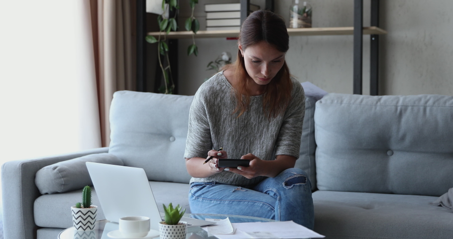 Woman sit on sofa in living room check household expenses, calculate bills use calculator laptop e-bank app, feels worried about financial problems. Not enough money for loan payment, eviction concept Royalty-Free Stock Footage #1056440081