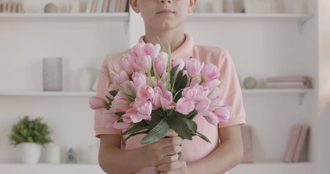 Unrecognizable boy stretching bouquet of pink tulips at camera. Polite Caucasian kid coming for holiday or birthday with flowers. Little gentleman giving gift and smiling.