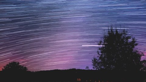 Star trail Time-lapse 4k footage of the stars behind a lone tree in the night sky. Milky Way galaxy orbiting over a mountain