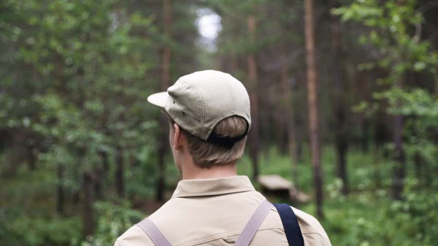 Close view from behind of blonde man with cap walking through forest