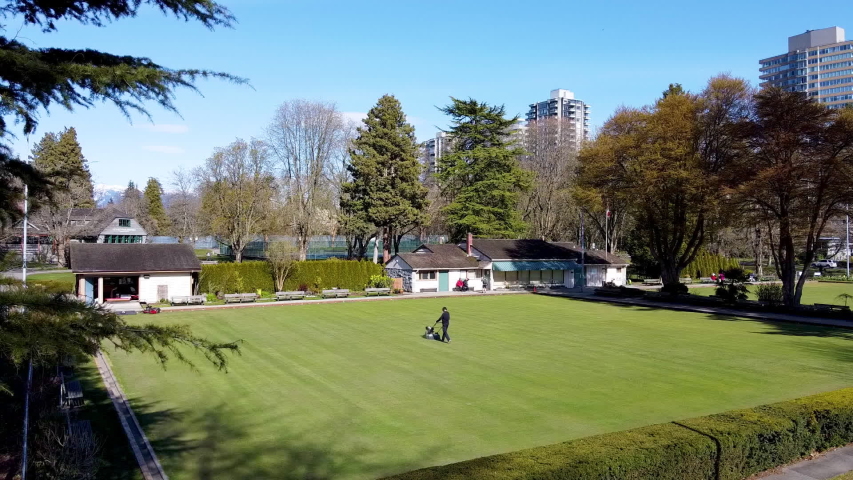 Aerial hold over Bocci Field in Stanley Park, Vancouver, British Columbia, Canada. During physical distancing. Groomer taking care of field, person walking away, while a couple watch on bench. 2-2