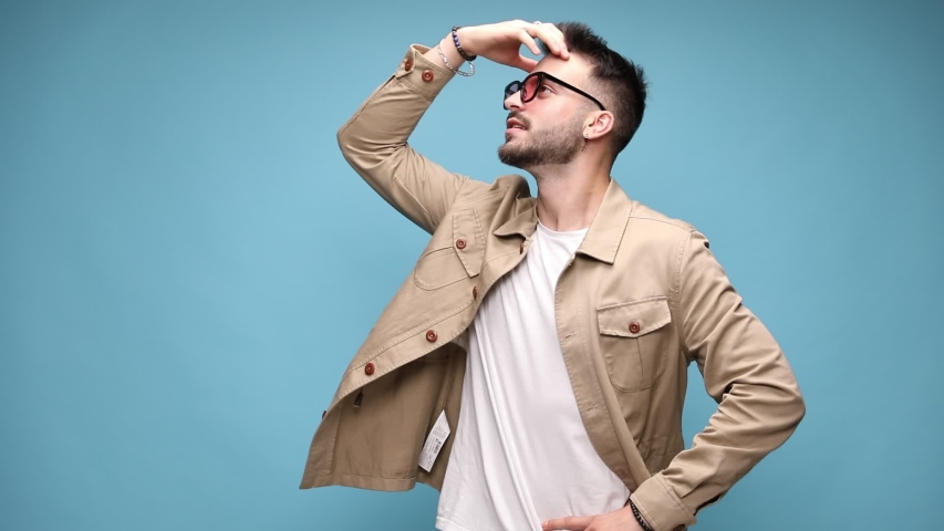 happy young casual guy holding hand to forehead thinking and trying to remember, pointing fingers and clapping, laughing and moving on blue background
