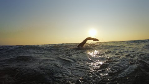 Professional swimmer man swimming front crawl in sea at sunset, slow motion