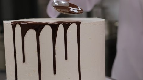 Close-up of a pastry chef pouring liquid chocolate on a white cream cake. The process of making a creamy cake with chocolate drips. The process of decorating the cake with liquid chocolate.
