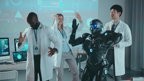 Black cyber robot prototype dancing with multi-ethnic team of scientists having fun repeating moves in the laboratory. Start-up success. Future. Robots and humans. Fun concept.