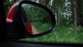 Video shooting in motion, view in the side mirror of a car, driving a red car along the road