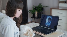 consultation of a veterinarian, caring girl loving her pet cat at veterinarians reception online using webcam on computer sitting on bed in room