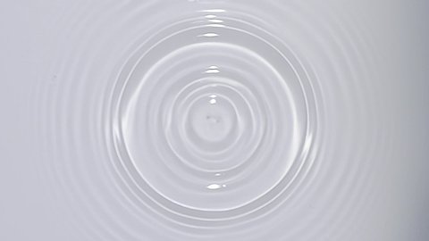Top view of drop falls into water and diverging circles of water on white background in slow motion