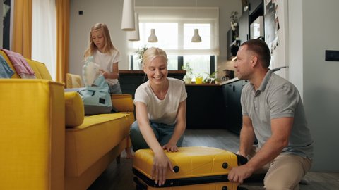 Happy family puts clothes in travel suitcase indoors of new home room. Smiling girl takes things for summer vacation. Beautiful mom closes baggage before departure or plane flight. Joy of family love