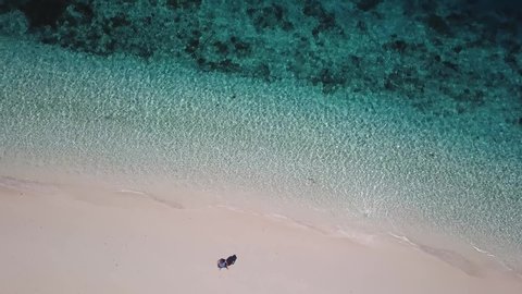 A drone shot of a man standing at the seashore of a white sand beach on a small island near Maumere, Indonesia. Happy and careless moments. Waves gently washing the shore. Adventure and discovery
